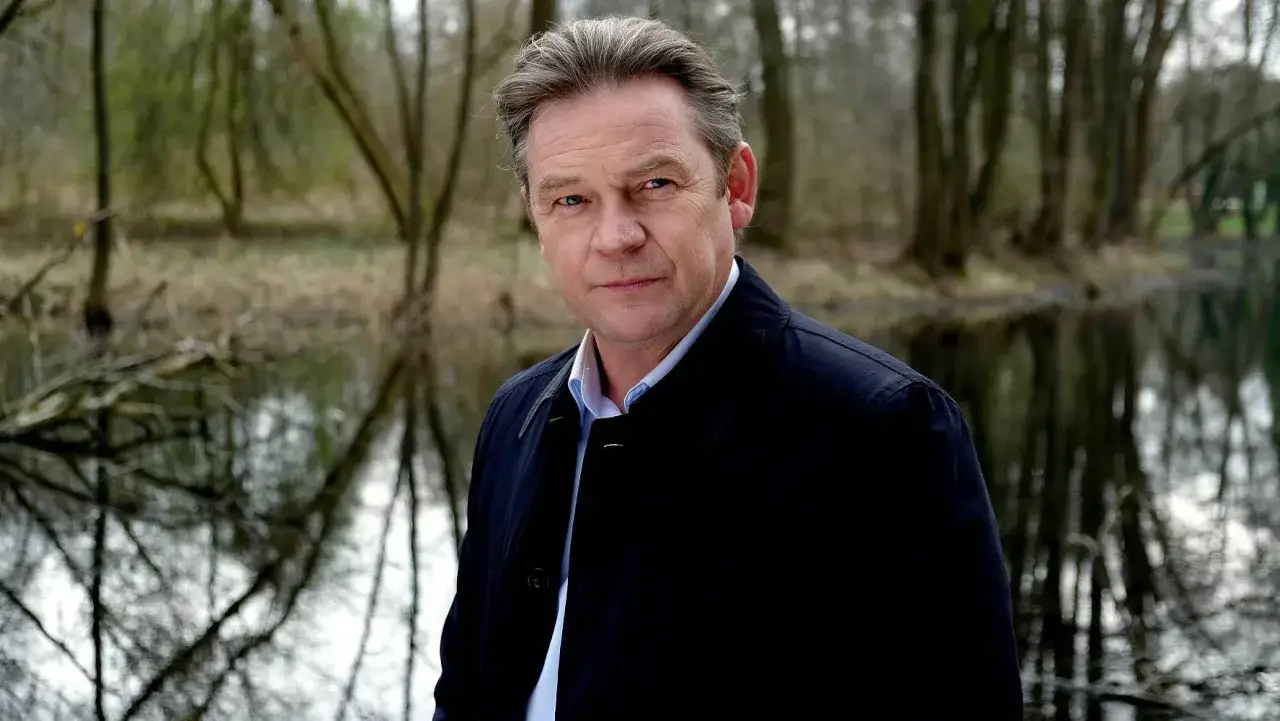 Ireneusz Czop, znany z film&oacute;w, seriali i program&oacute;w, pozuje nad wodą w otoczeniu drzew.