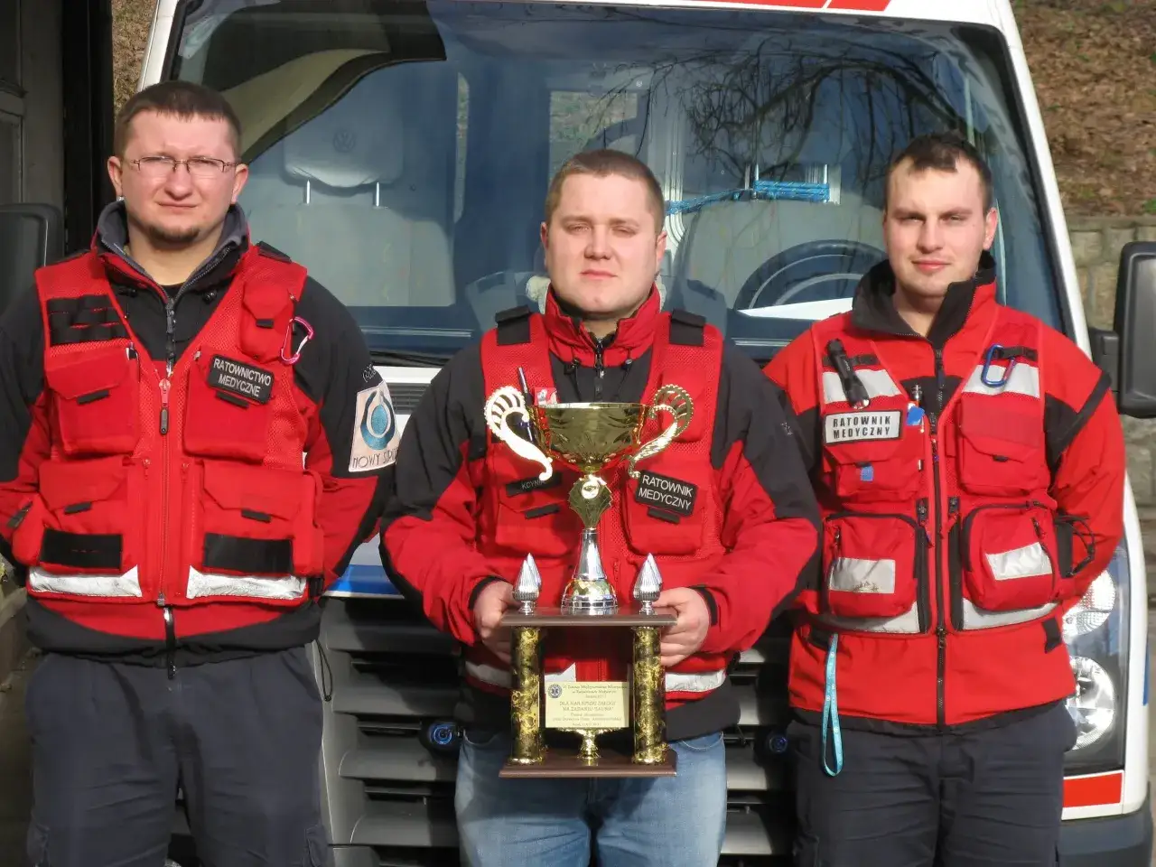 Trzech ratowników medycznych w czerwonych kamizelkach, jeden z nich trzyma puchar. To oni mogą prowadzić kurs pierwszej pomocy.