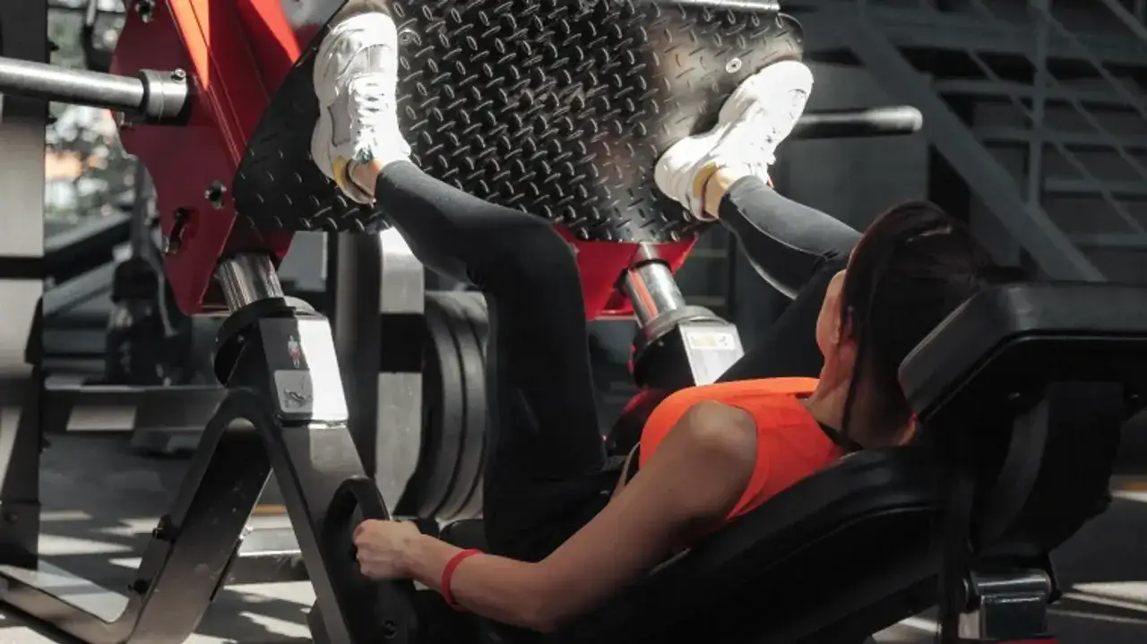 Kobieta ćwiczy na maszynie do wyciskania n&oacute;g, wykonując ruchy push & pull.