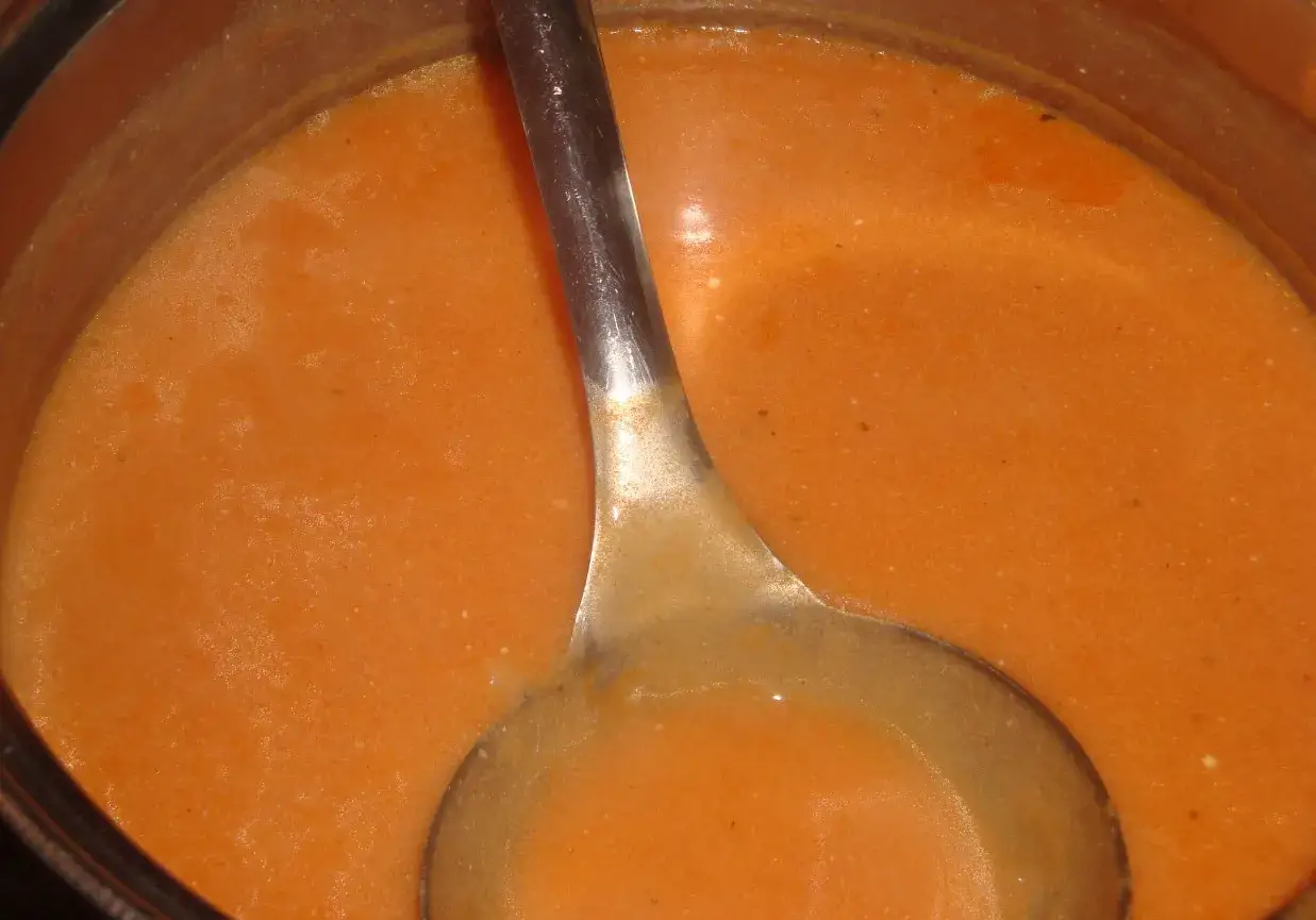 Gęsty, pomarańczowy sos do gołąbk&oacute;w w garnku, z metalową chochlą zanurzoną w środku.