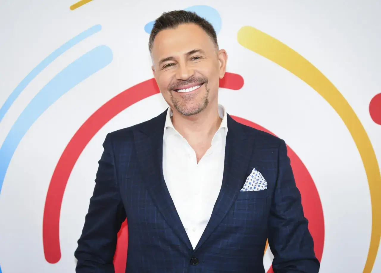 Uśmiechnięty Krzysztof Ibisz w garniturze, którego styl i elegancja sugerują jego spory majątek.