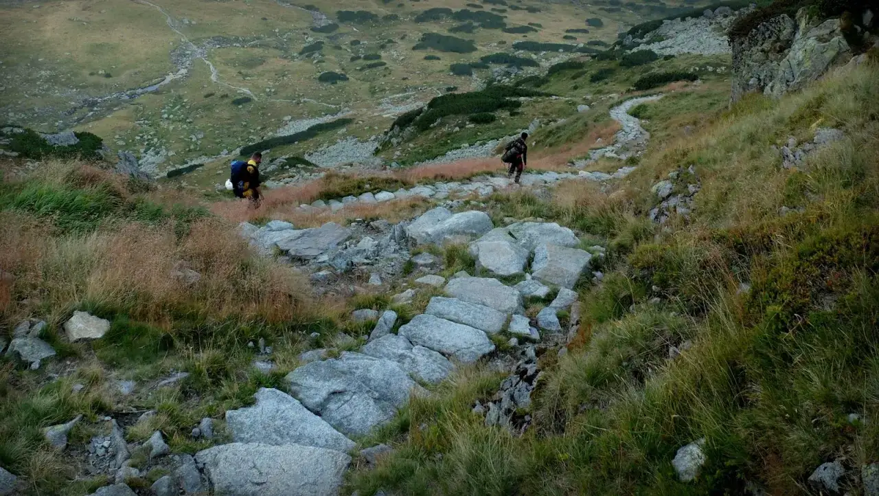 Dwóch turystów pokonuje kamienisty szlak, jeden z nich schodzi, drugi wspina się. To mogą być najtrudniejsze szlaki w Tatrach.