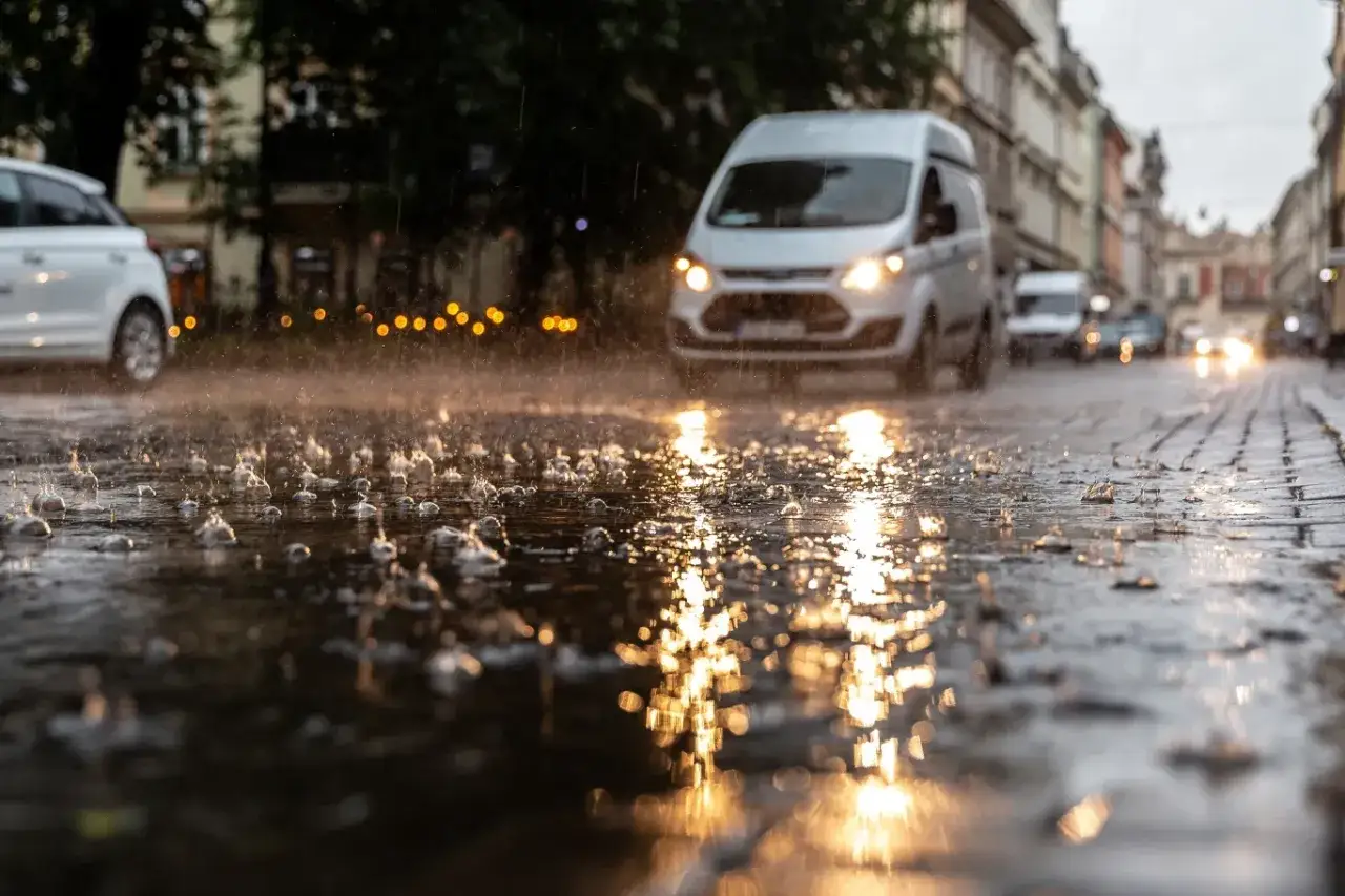 Deszcz na ulicy, odbijające się światła mijania i dzienne samochod&oacute;w na mokrej nawierzchni.