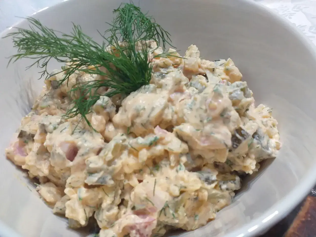 Pyszna sałatka ziemniaczana z boczkiem, og&oacute;rkiem kiszonym i koperkiem, podana w białej misce.