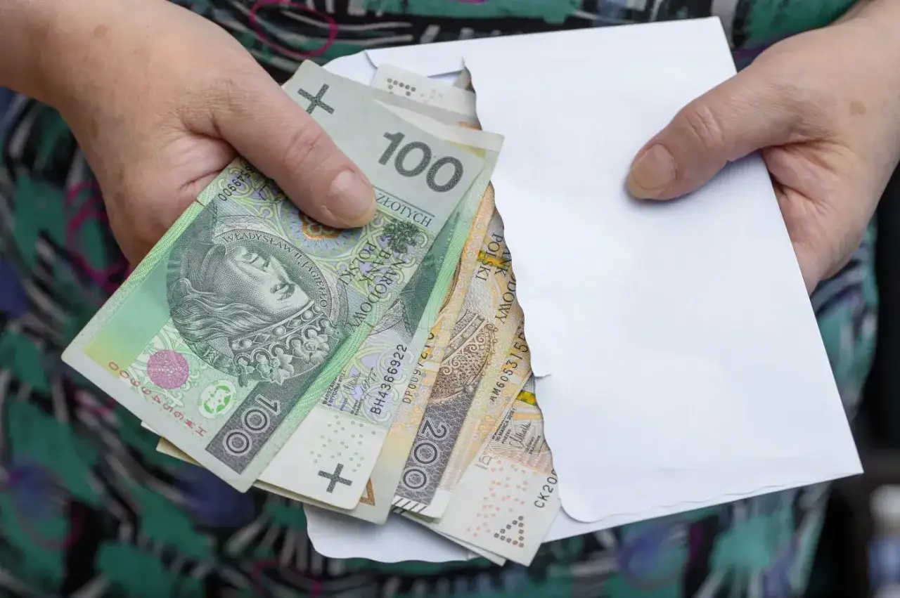 Ręce trzymają kopertę z polskimi banknotami. Czy komornik może zająć rentę rodzinną na dziecko?
