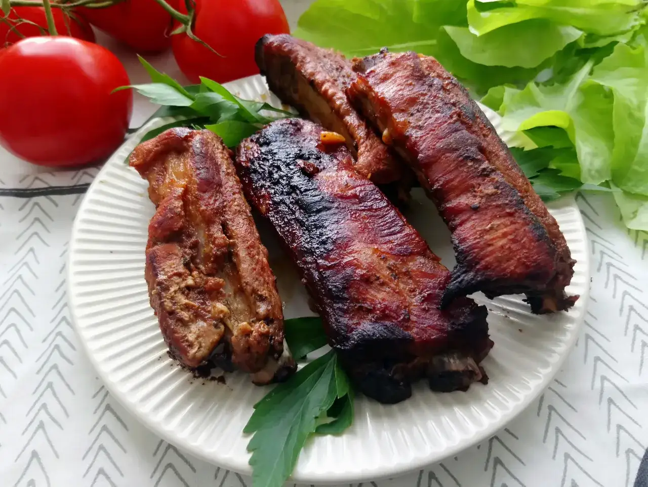 Pyszne żeberka w coli, lekko przypieczone, podane z pomidorami i sałatą.