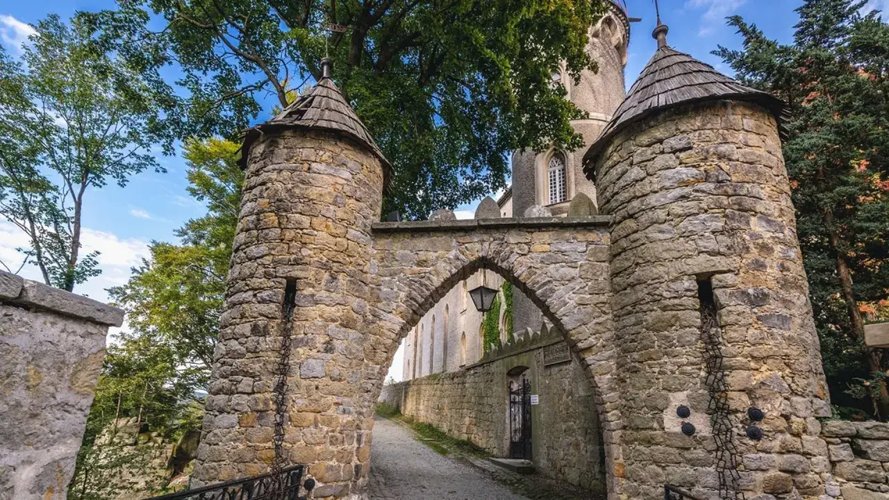 Kamienne wieże i łuk bramy wjazdowej do zamku Leśna Skała. W oddali widać fragment murów i drzewa.