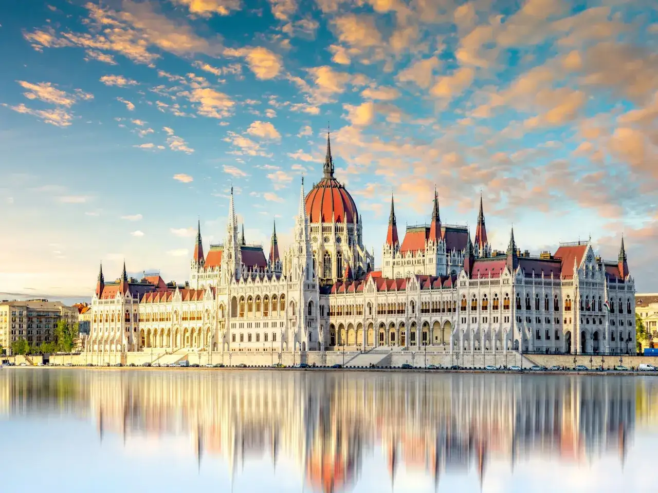 Budynek Parlamentu w Budapeszcie odbijający się w Dunaju to jeden z punktów, co warto zobaczyć na Węgrzech. Zachód słońca maluje niebo na pomarańczowo.