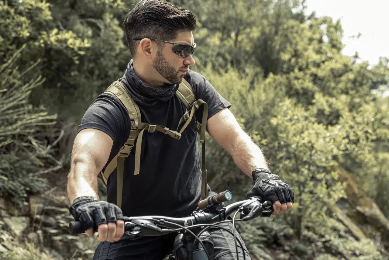 Mężczyzna w okularach rowerowych i rękawiczkach trzyma kierownicę roweru, gotowy na jazdę po leśnym szlaku.