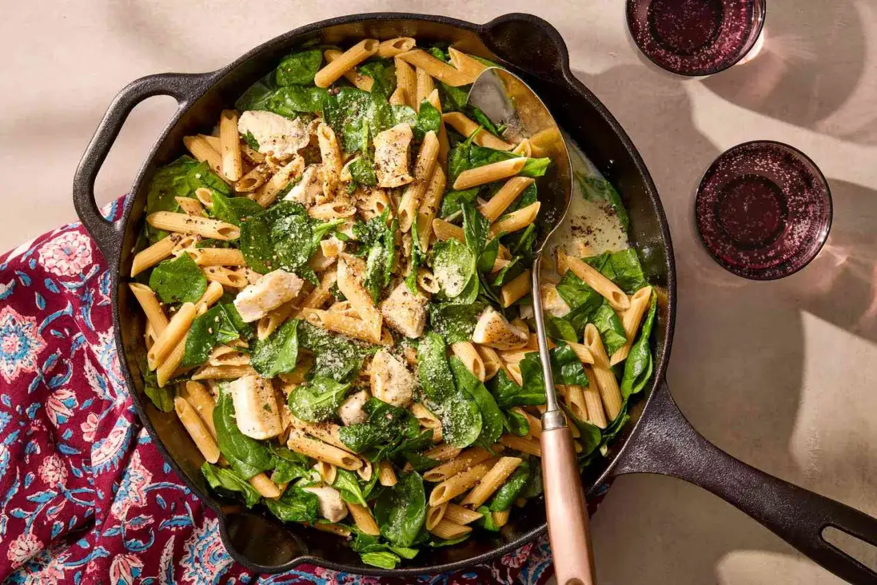 Szybki obiad z makaronem penne, kurczakiem i szpinakiem w sosie śmietanowym, posypany parmezanem, podany w żeliwnej patelni.