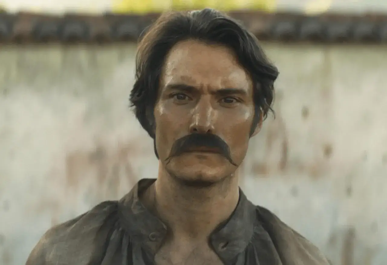 Mężczyzna z bujnymi wąsami, w brązowej koszuli, wygląda jak postać z serialu 