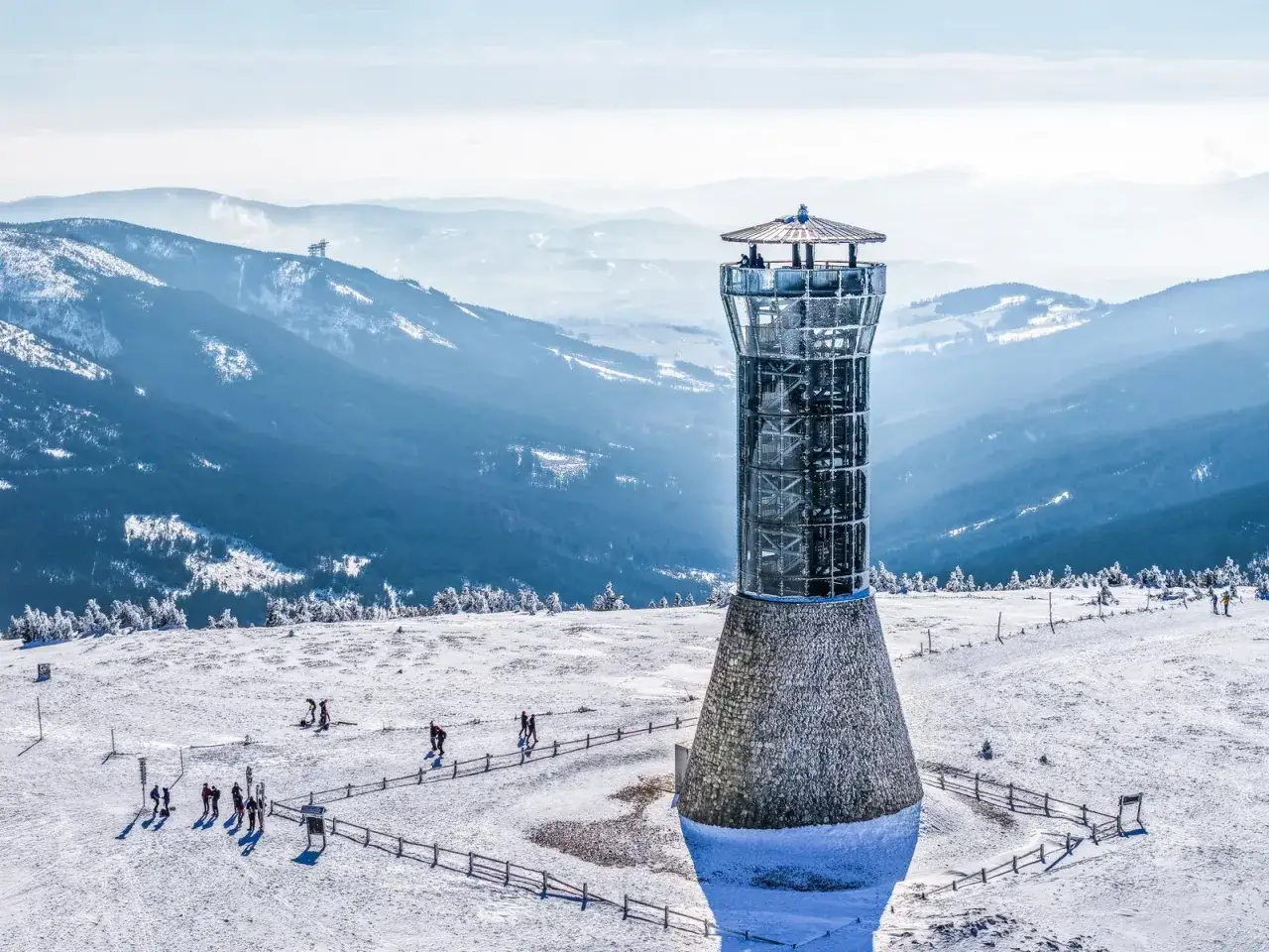 Wieża widokowa Tr&oacute;jmorski Wierch w zimowej scenerii. Ludzie spacerują po ośnieżonym szczycie, podziwiając g&oacute;rskie krajobrazy.