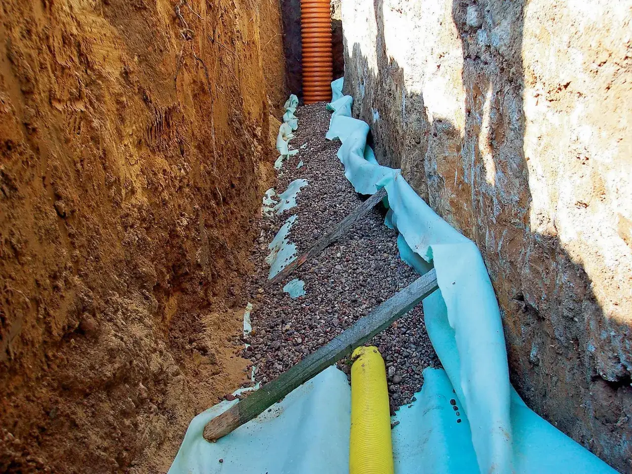 Budowa drenażu: jak głęboko zakopać rury drenażowe, by skutecznie odprowadzały wodę. Widoczny wykop z kruszywem i geowłókniną.