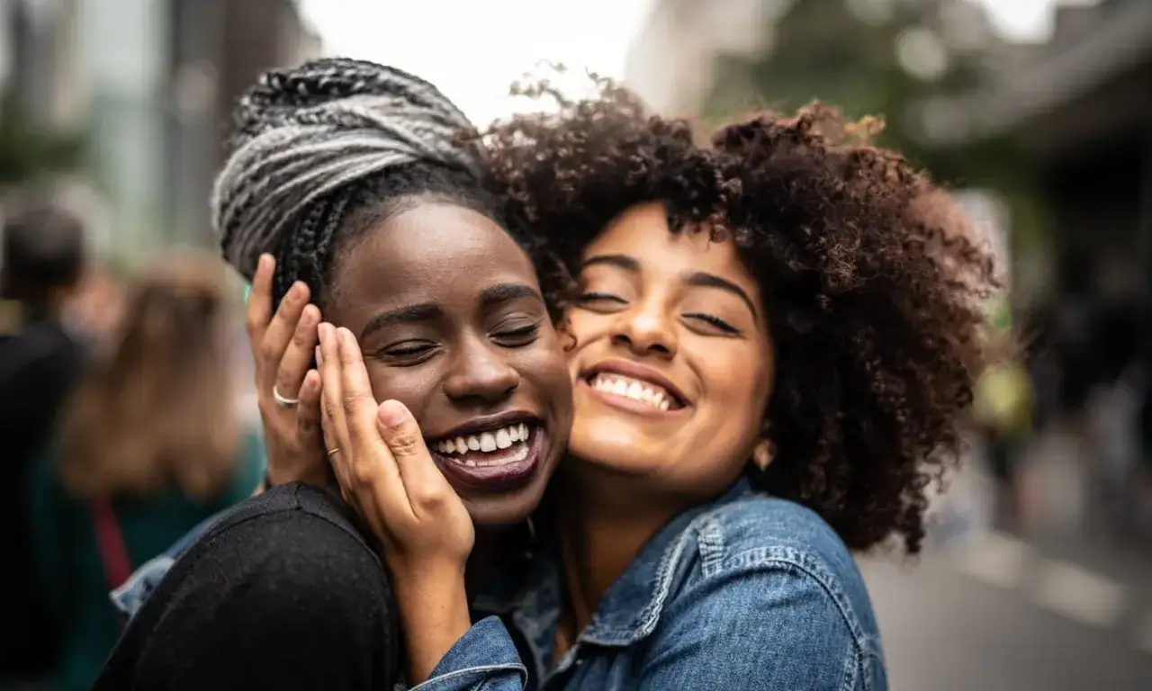 Dwie przyjaci&oacute;łki śmieją się radośnie, przytulając się. Jedna z nich ma warkocze, druga kręcone włosy. Dziękuję, że jesteś w moim życiu.