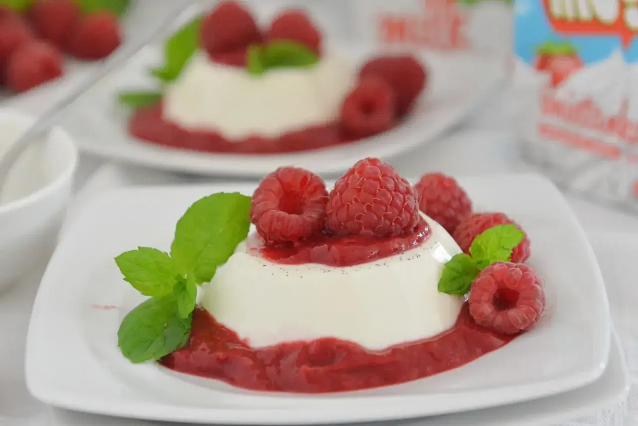 Panna cotta z malinowym sosem i świeżymi malinami, ozdobiona listkami mięty. Idealny deser na letnie popołudnie.