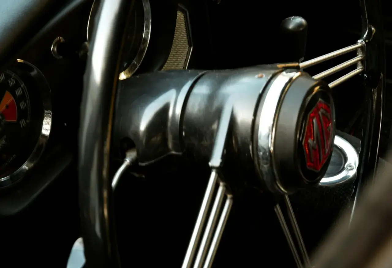 Kierownica klasycznego MG, z metalicznym piskiem przy skręcaniu. Widoczny emblemat MG i fragment licznika.