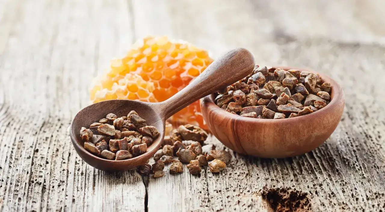 Propolis co to? Złocisty plaster miodu i drewniana łyżka pełna drobnych, brązowych grudek propolisu na rustykalnym tle.