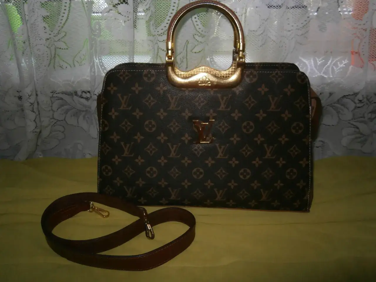 Elegancka, duża torebka Louis Vuitton z monogramem i złotymi elementami. Obok leży dopasowany, brązowy pasek.