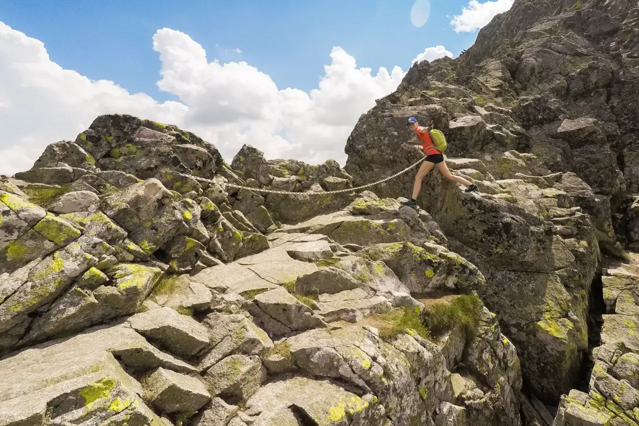 Kobieta wspina się po skalistej trasie na Kozi Wierch, trzymając się łańcucha.