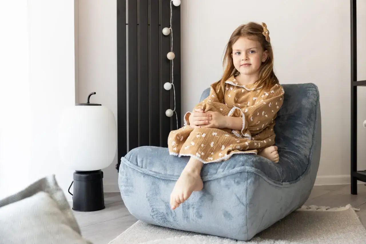 Uśmiechnięta dziewczynka w piżamce siedzi na miękkim, niebieskim fotelu dla dziecka.