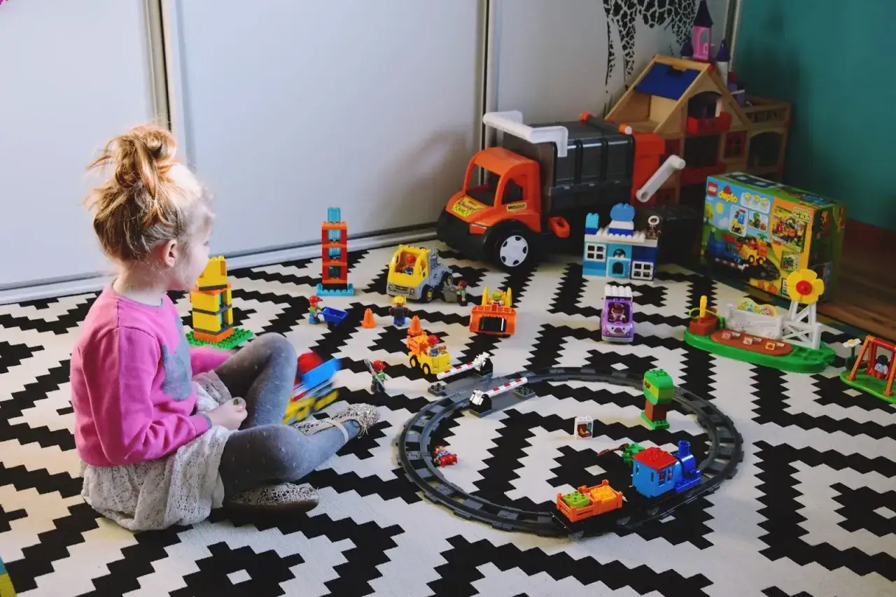 Dziewczynka bawi się klockami Duplo, tworząc scenki z życia budowy i kolei. To idealne kreatywne zabawy z dwulatkiem.