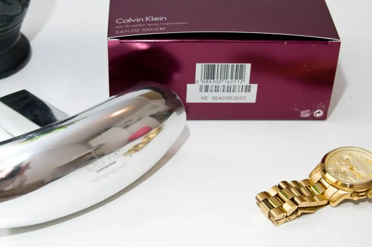 Perfumy Calvin Klein, pudełko z kodem kreskowym i numerem seryjnym. Jak sprawdzić oryginalność? Złoty zegarek obok.