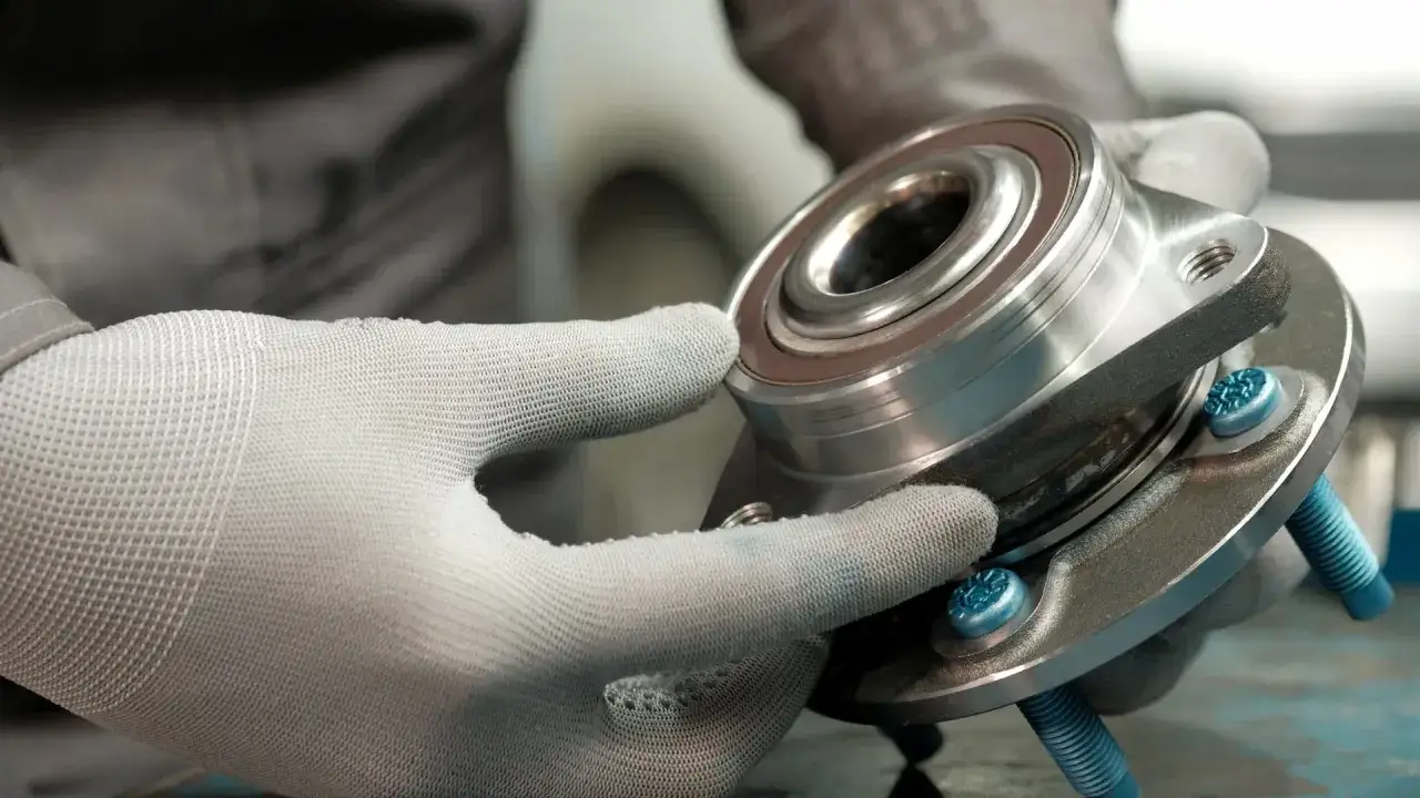 Mechanik w rękawiczkach sprawdza nowe łożysko koła, przygotowując się do jego wymiany.