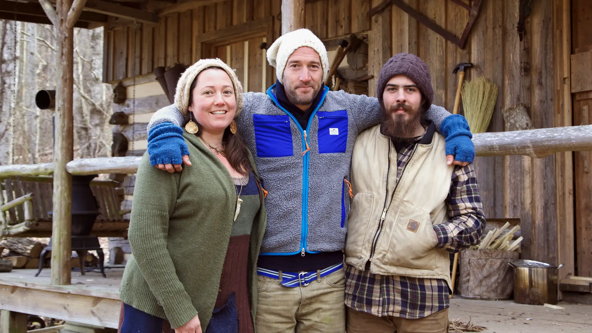 Trzy osoby stoją przy drewnianej chacie. Witamy na odludziu, gdzie czas płynie wolniej.