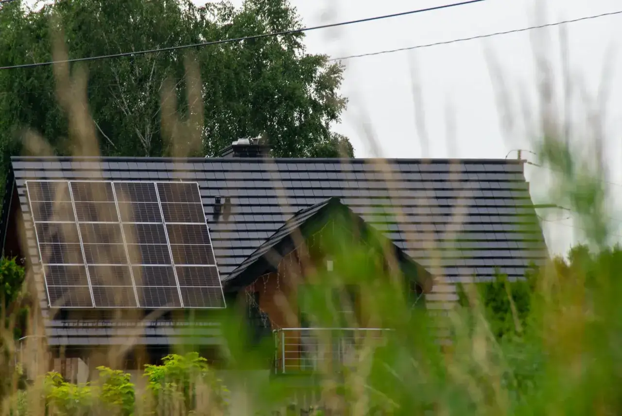 Panele fotowoltaiczne na dachu domu, być może instalacja fotowoltaiczna bez zgłoszenia, otoczone zielenią.