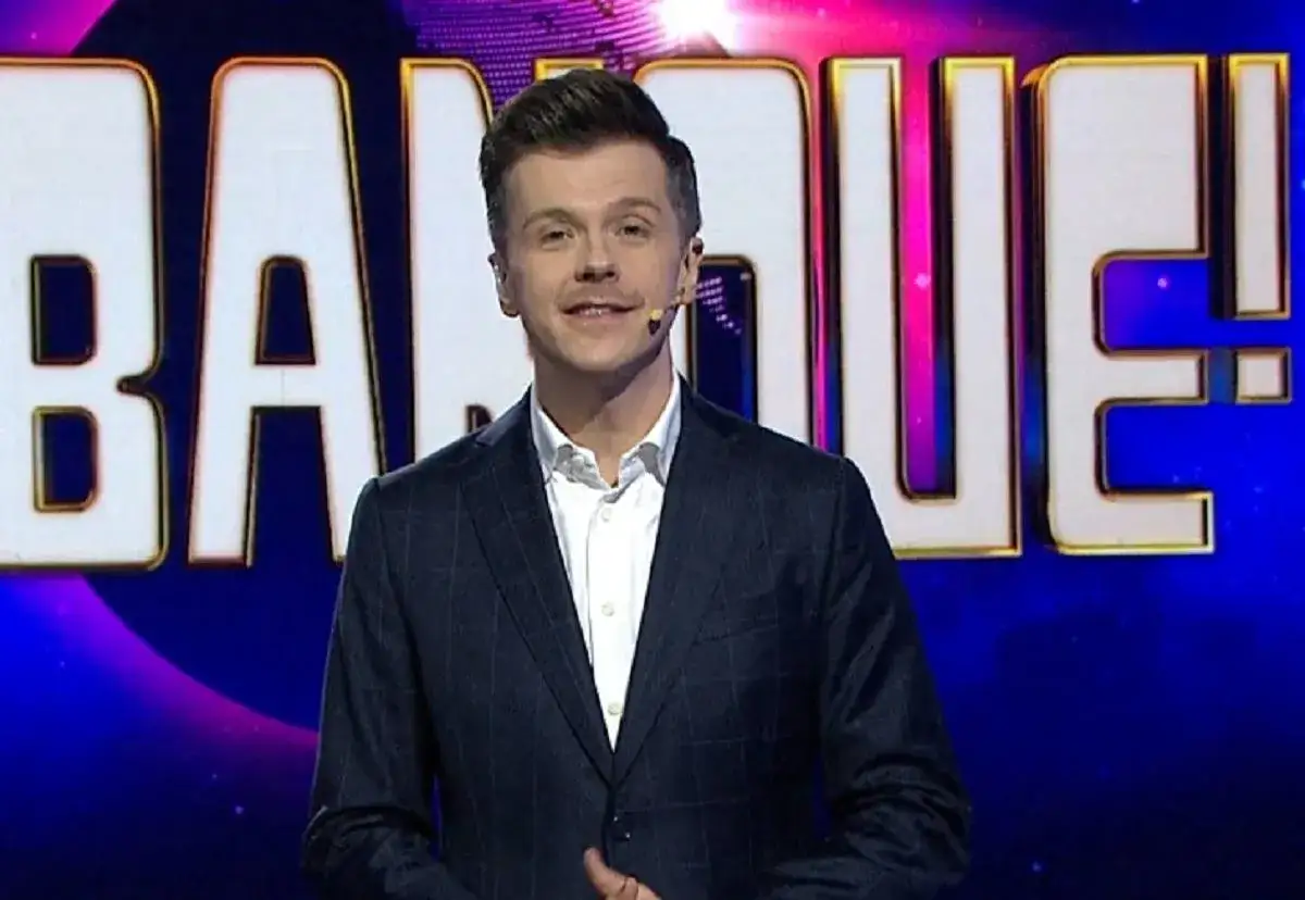 Mężczyzna w garniturze, kt&oacute;ry prowadzi vabank, uśmiecha się na tle napisu 