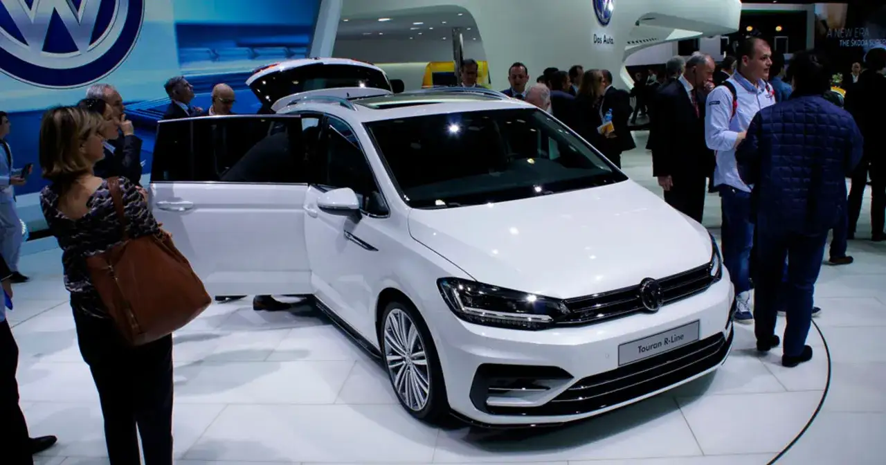 Biały Volkswagen Touran R-Line na wystawie, z otwartymi drzwiami i bagażnikiem. Ludzie oglądają nowy model.
