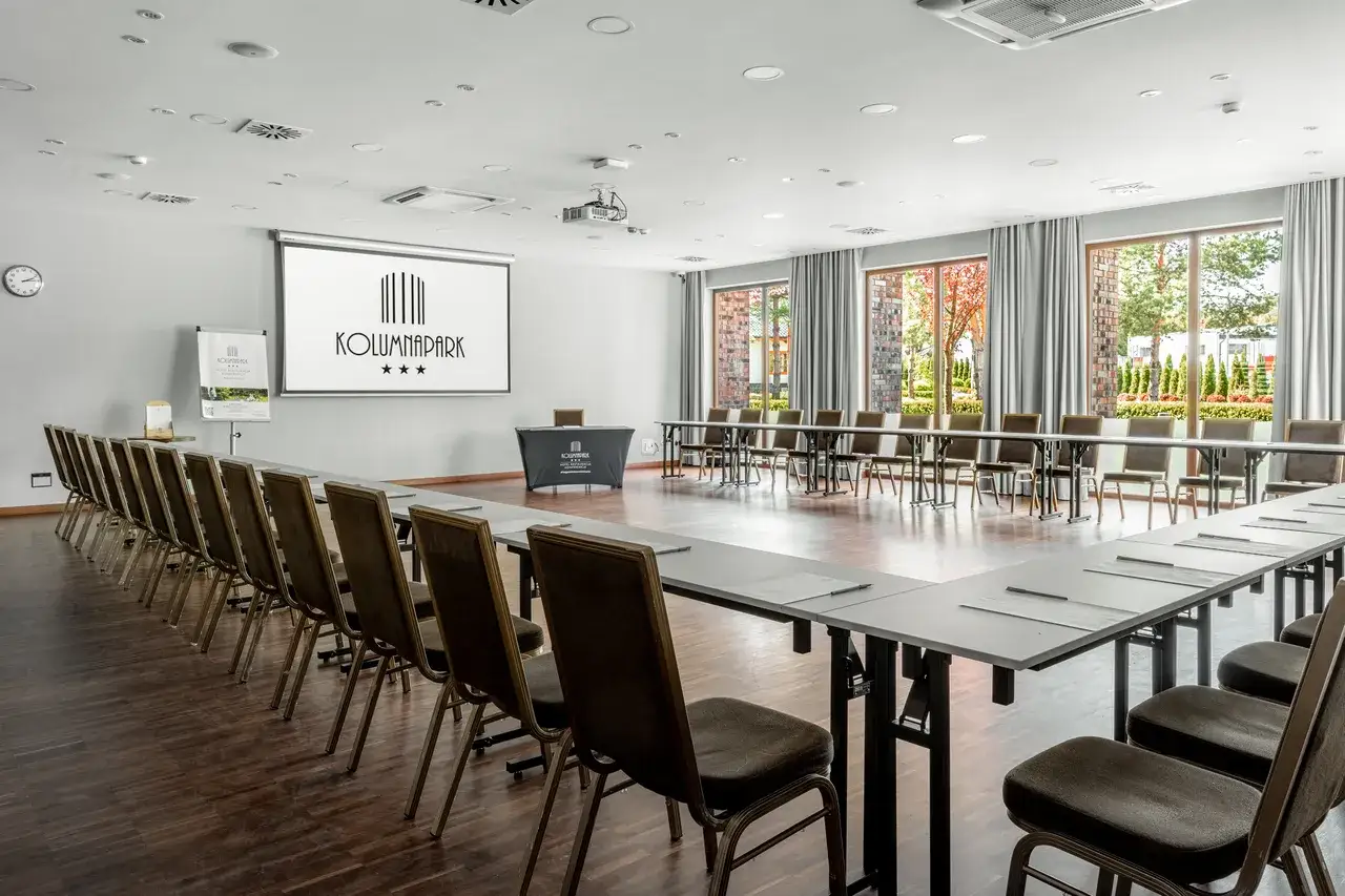 Sala konferencyjna w hotelu Kolumna Park, gotowa na spotkanie. Ustawienie w kształt podkowy, z ekranem projekcyjnym i wygodnymi krzesłami.