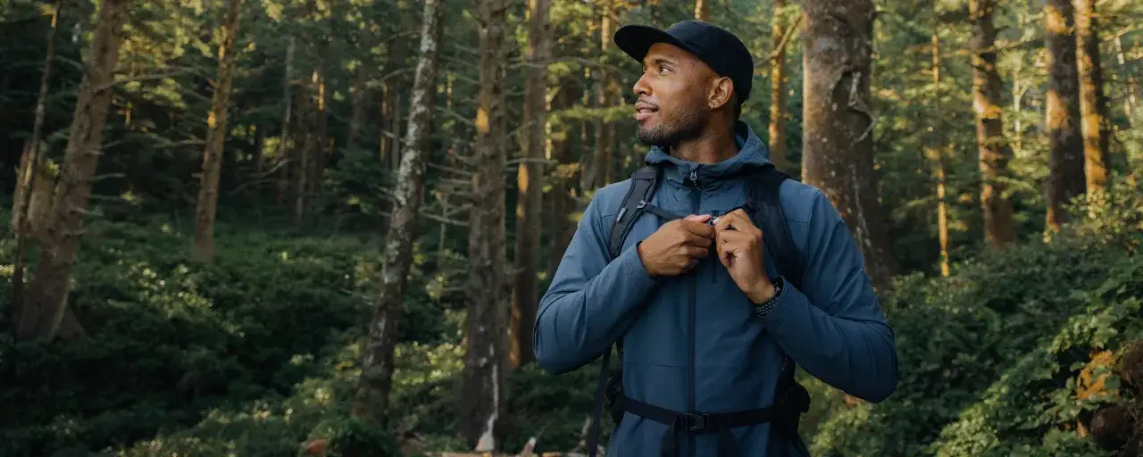 Mężczyzna w lesie zapina kurtkę softshell. Co to znaczy? To lekka, oddychająca odzież na zmienną pogodę.