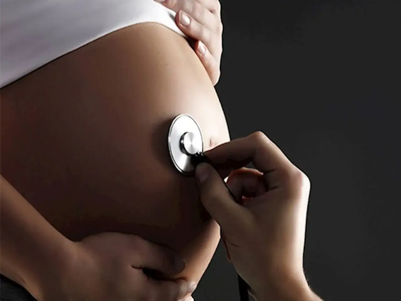 Dłoń z fonendoskopem na brzuchu ciężarnej. Czy nospa w ciąży jest bezpieczna? Konsultacja lekarska jest kluczowa.