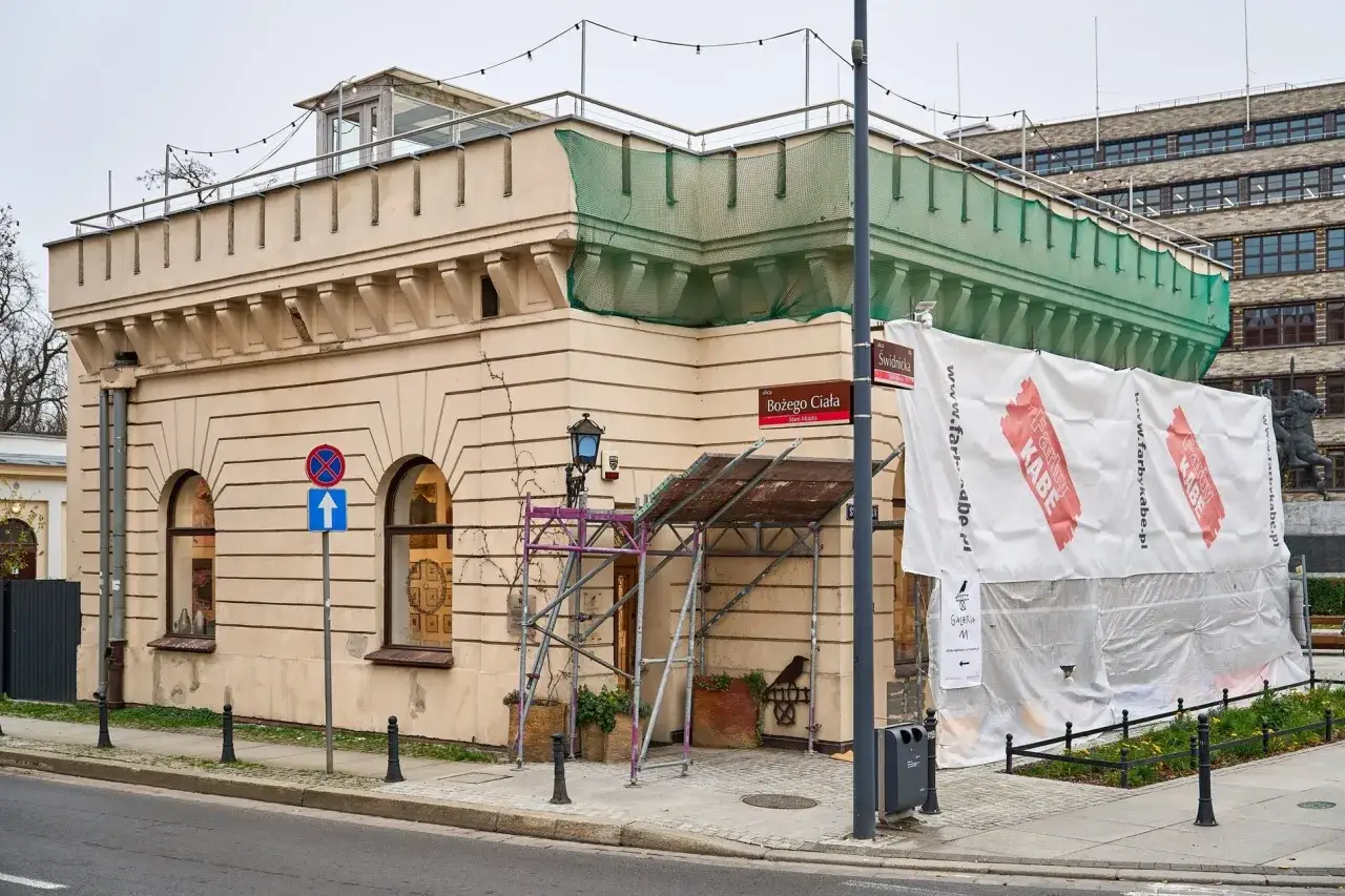 Budynek z charakterystyczną attyką i łukowymi oknami, częściowo zakryty płachtą. Czy ma ile lat musi mieć budynek żeby był zabytkiem?