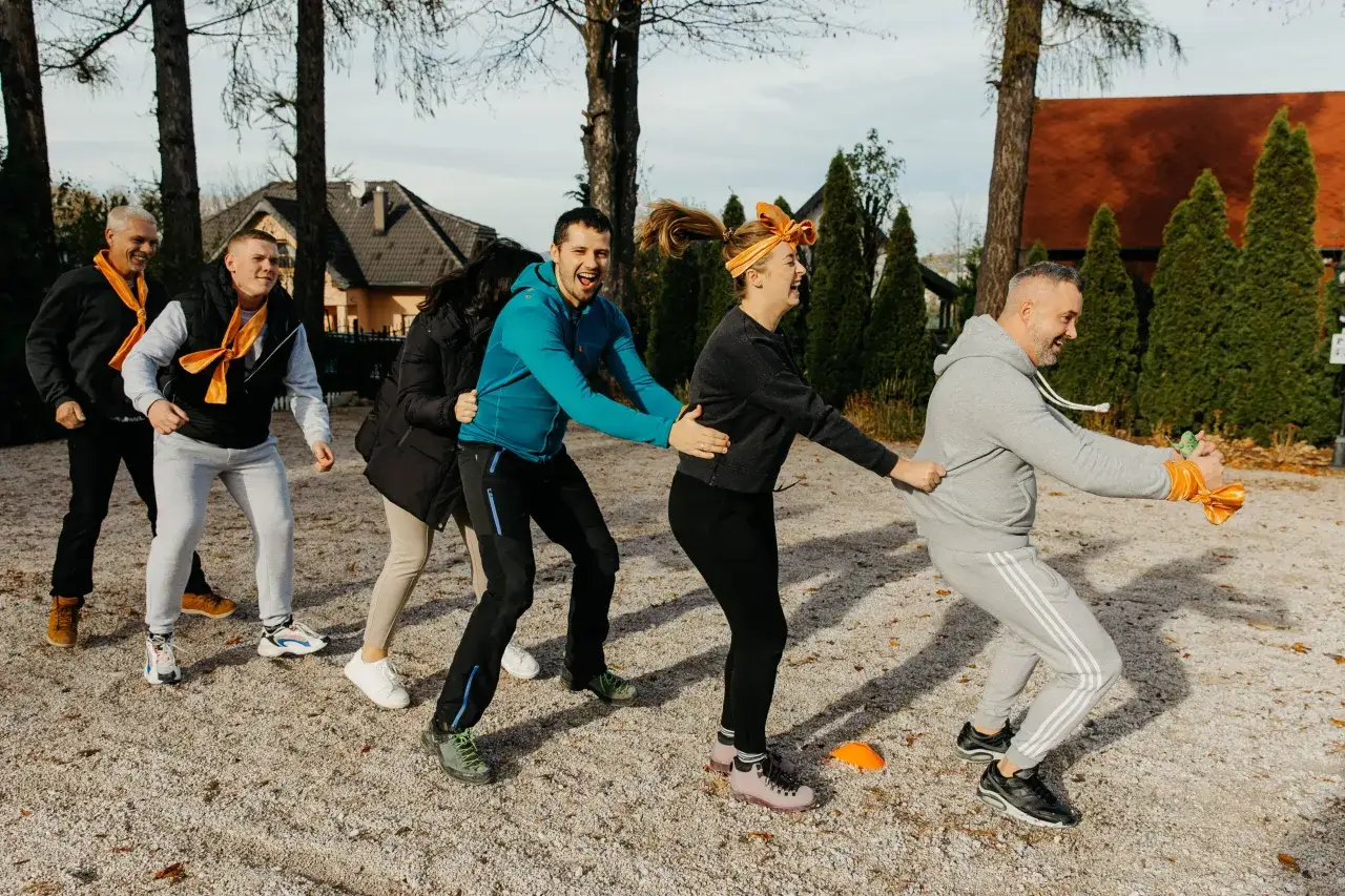 Grupa ludzi w pomarańczowych szalikach bierze udział w kreatywnych zabawach dla młodzieży na świeżym powietrzu, śmiejąc się i bawiąc.