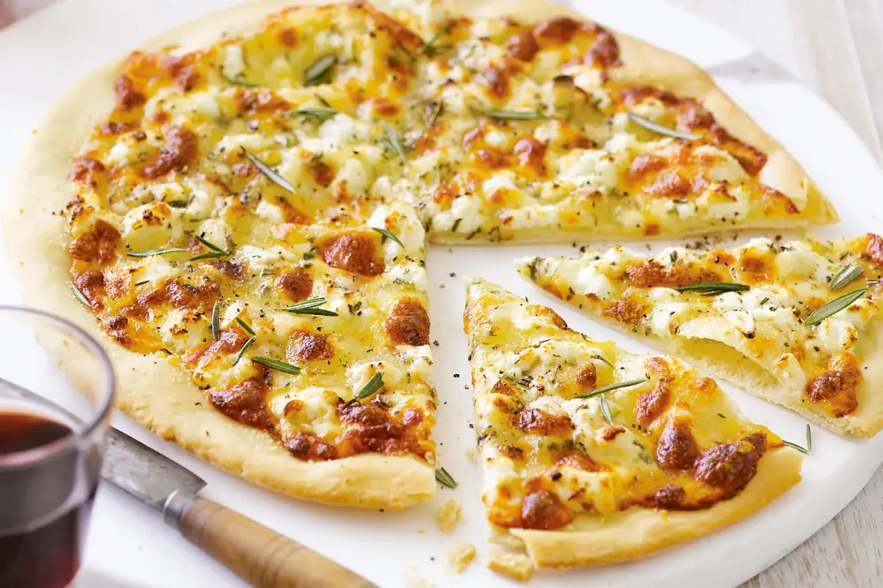 Pyszna pizza bianca z serem i rozmarynem, pokrojona na kawałki, obok kieliszka czerwonego wina i noża.