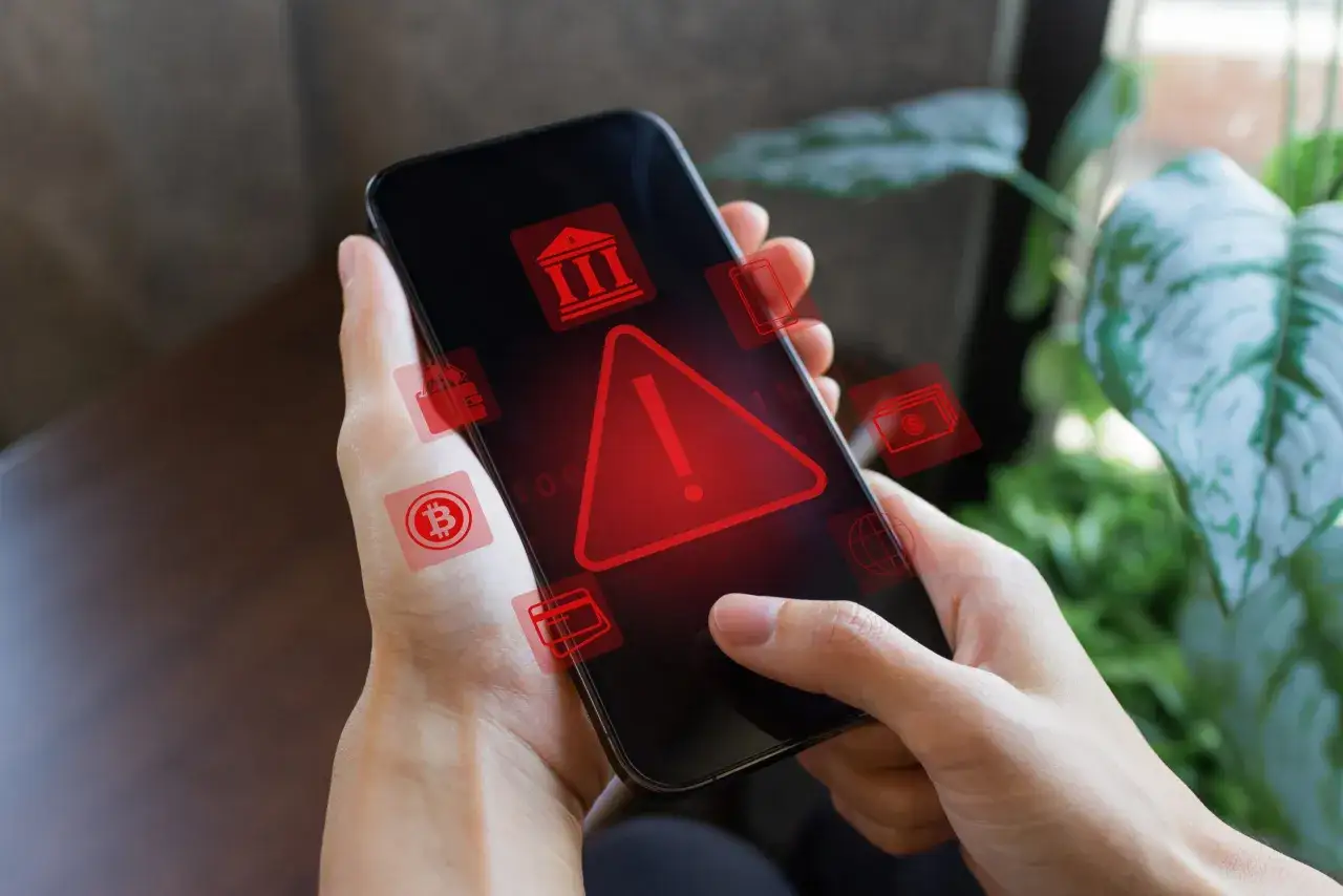 Smartfon z różnymi ikonami aplikacji do kryptowalut, niektóre z czerwoną flagą ostrzegawczą