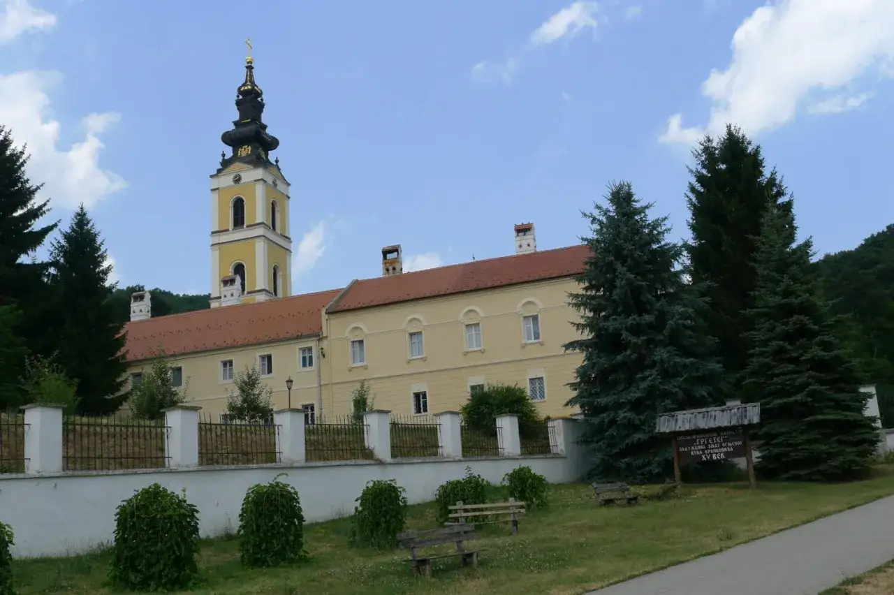Klasztor Grgeteg na Fruskiej Gorze, z charakterystyczną żółtą wieżą i czerwoną dachem, otoczony zielenią.