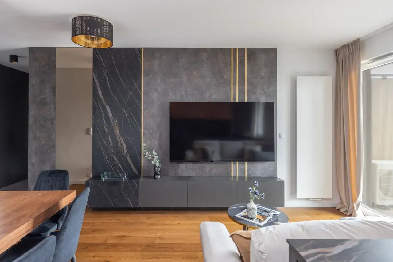 Nowoczesna ściana telewizyjna z tapetą imitującą marmur i złotymi akcentami. Elegancka, stylowa przestrzeń.