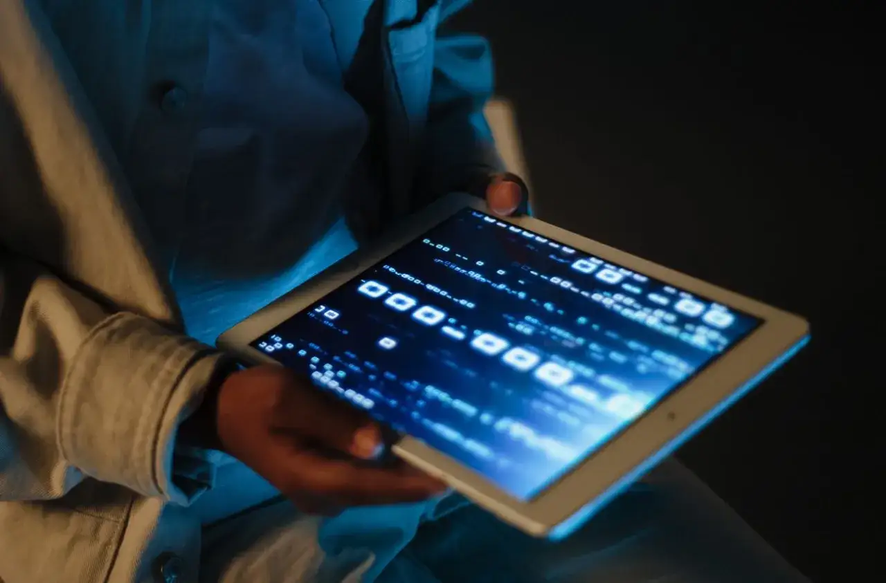 Osoba trzyma tablet z kodem binarnym na ekranie, szukając informacji, jak zresetować tablet gdy jest zablokowany.
