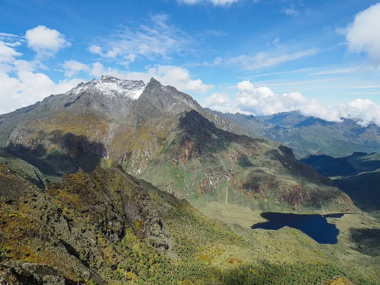 Majestatyczna g&oacute;ra Stanleya, ośnieżony szczyt i skaliste zbocza, w dole ciemne jezioro i zielone doliny.