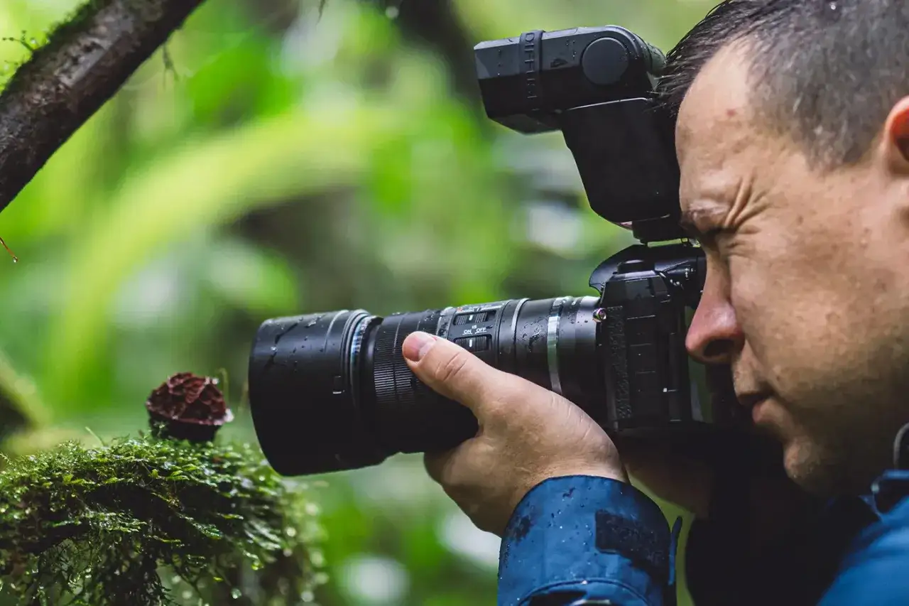 Fotograf z aparatem i lampą błyskową przygląda się grzybowi na mchu. Idealny obiektyw do zdjęć z bliska.