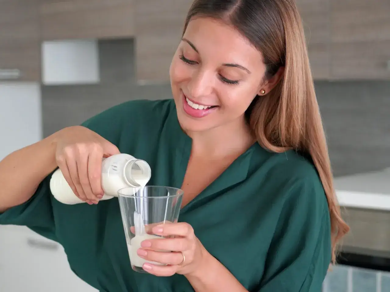 Uśmiechnięta kobieta nalewa kefir do szklanki. Czy kefir jest dobry na odchudzanie? To zdrowy nap&oacute;j, kt&oacute;ry może wspom&oacute;c dietę.