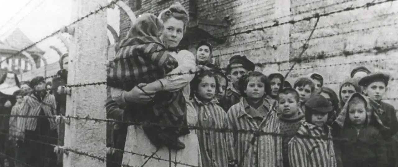 Dzieci w pasiakach za drutem kolczastym, obraz przypominający sceny z książek o Auschwitz.