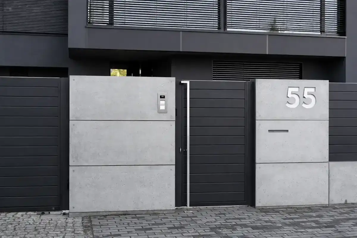 Nowoczesne ogrodzenie murowane pełne z betonowych płyt, z szarą bramą i numerem 55.