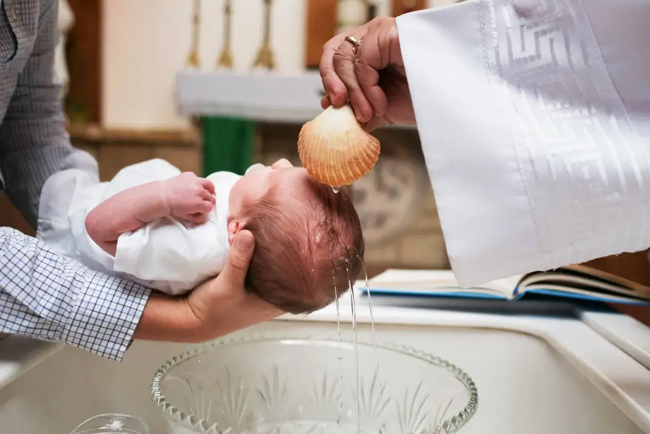 Chrzest bez mszy: niemowlę trzymane nad misą, kapłan polewa mu głowę wodą z muszli.