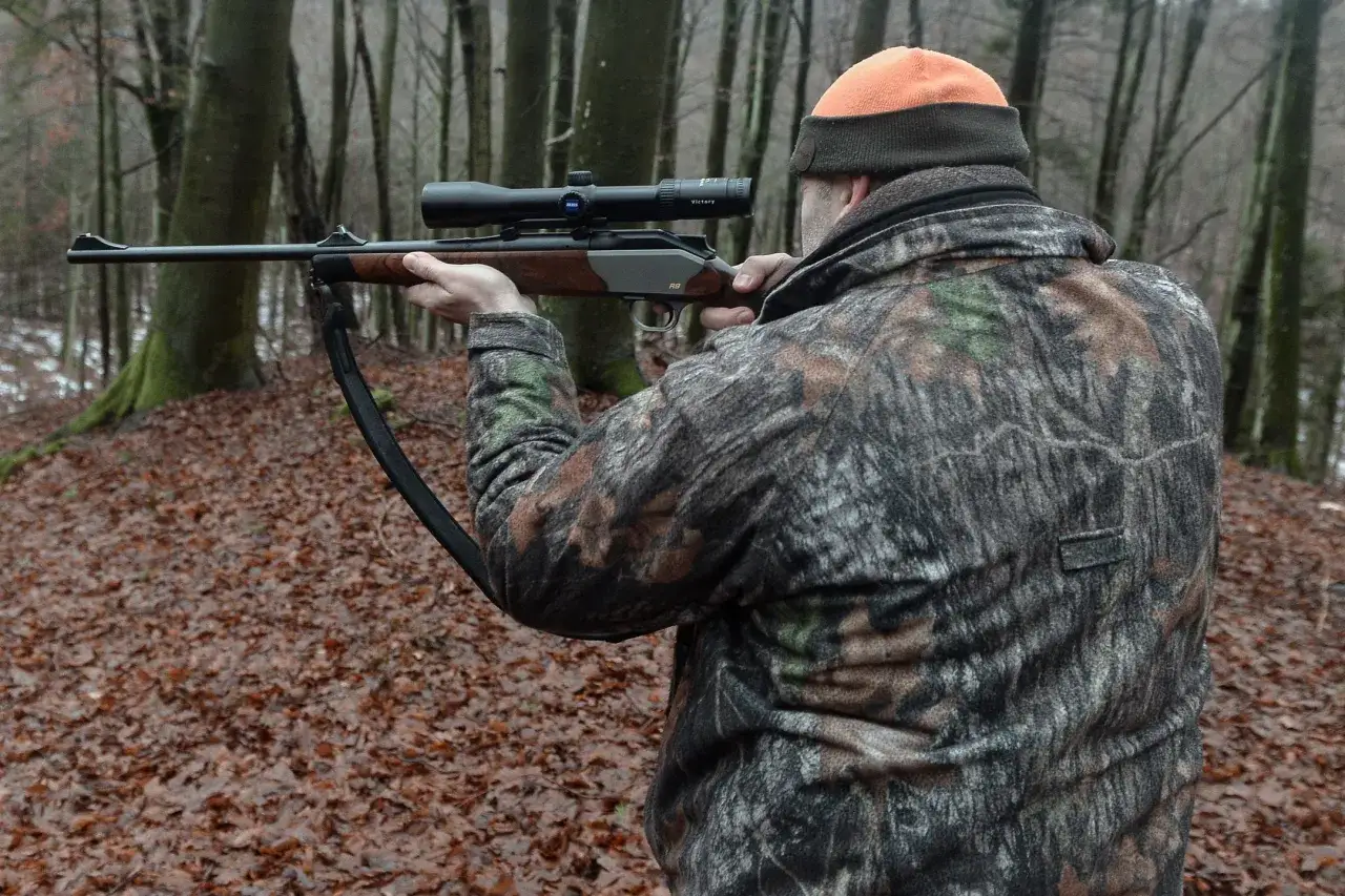 Myśliwy w kamuflażu celuje z broni. Czy myśliwy może użyć broni w obronie własnej? Las jesienią, opadłe liście.
