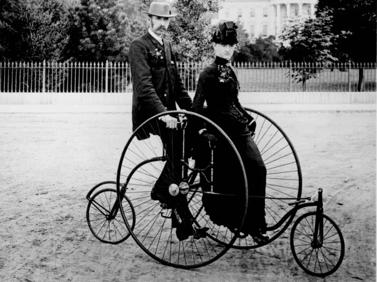 Para, jak wyglądał pierwszy rower: mężczyzna i kobieta na welocypedzie z ogromnym przednim kołem i małym tylnym.