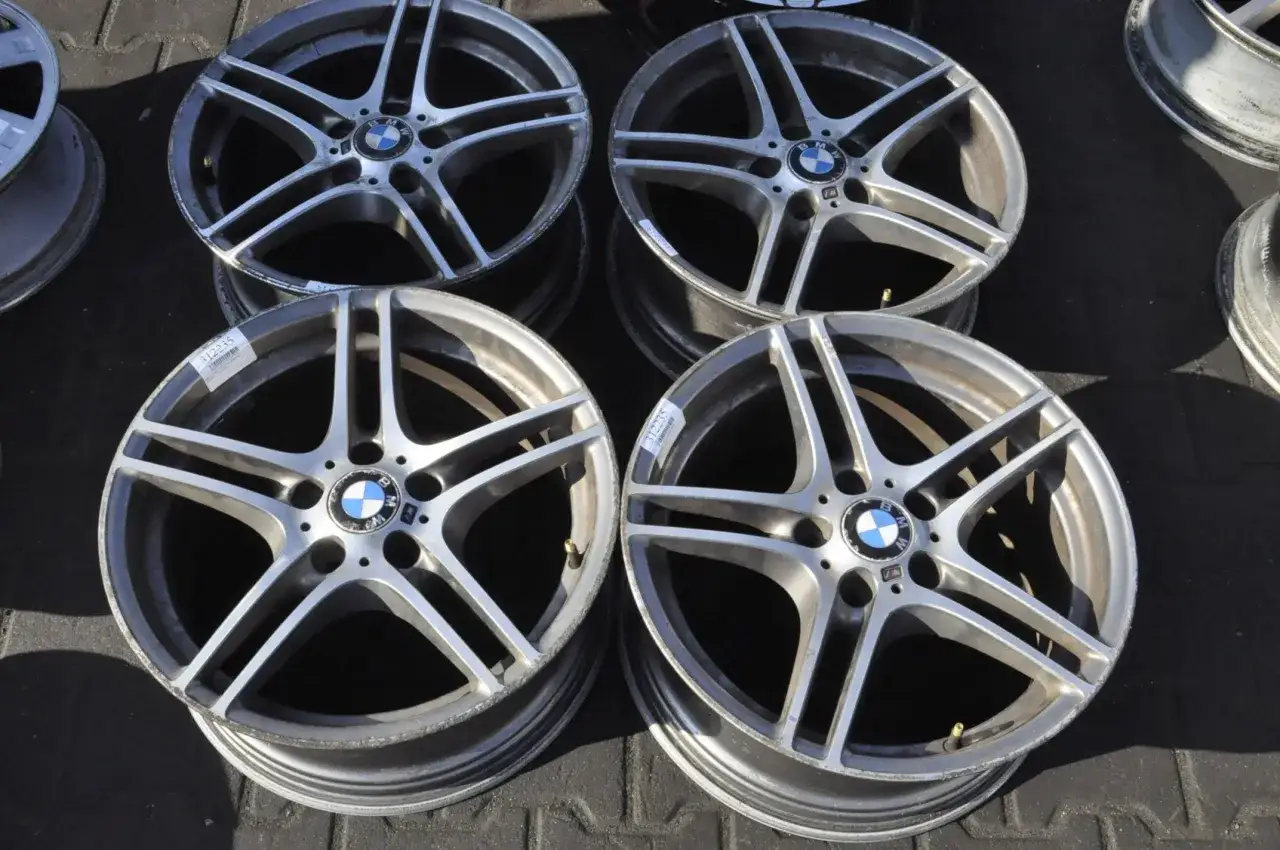 Cztery felgi BMW styling wheels, każda z pięcioma podwójnymi ramionami, leżą na ciemnej powierzchni.